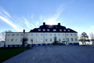 Bilden visar Rimforsa strand. En gul herrgårdsliknande hotellbyggnad i Rimforsa vid sjön Åsunden i Östergötland